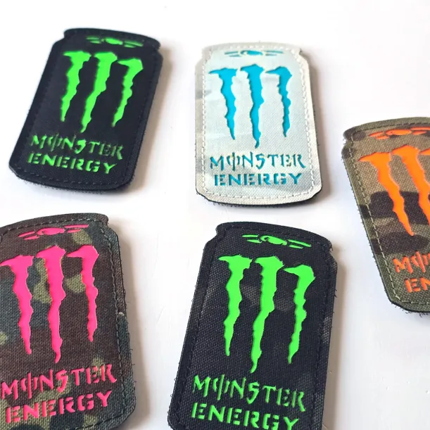 Three Monster Energy laser cut Cordura Velcro patches: black with neon green, white with turquoise, and camouflage with orange details.